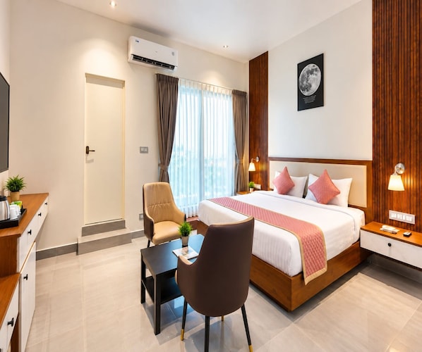 A hotel room with a bed, bedside tables, a desk, a chair, and a window with curtains. - Deluxe Room V Stays (Chittoor)