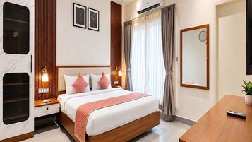 A hotel room with a bed, bedside tables, a desk, a mirror, and an air conditioning unit.