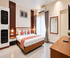 A hotel room with a bed, bedside tables, a desk, a mirror, and an air conditioning unit. - Deluxe Room V Stays (Chittoor)