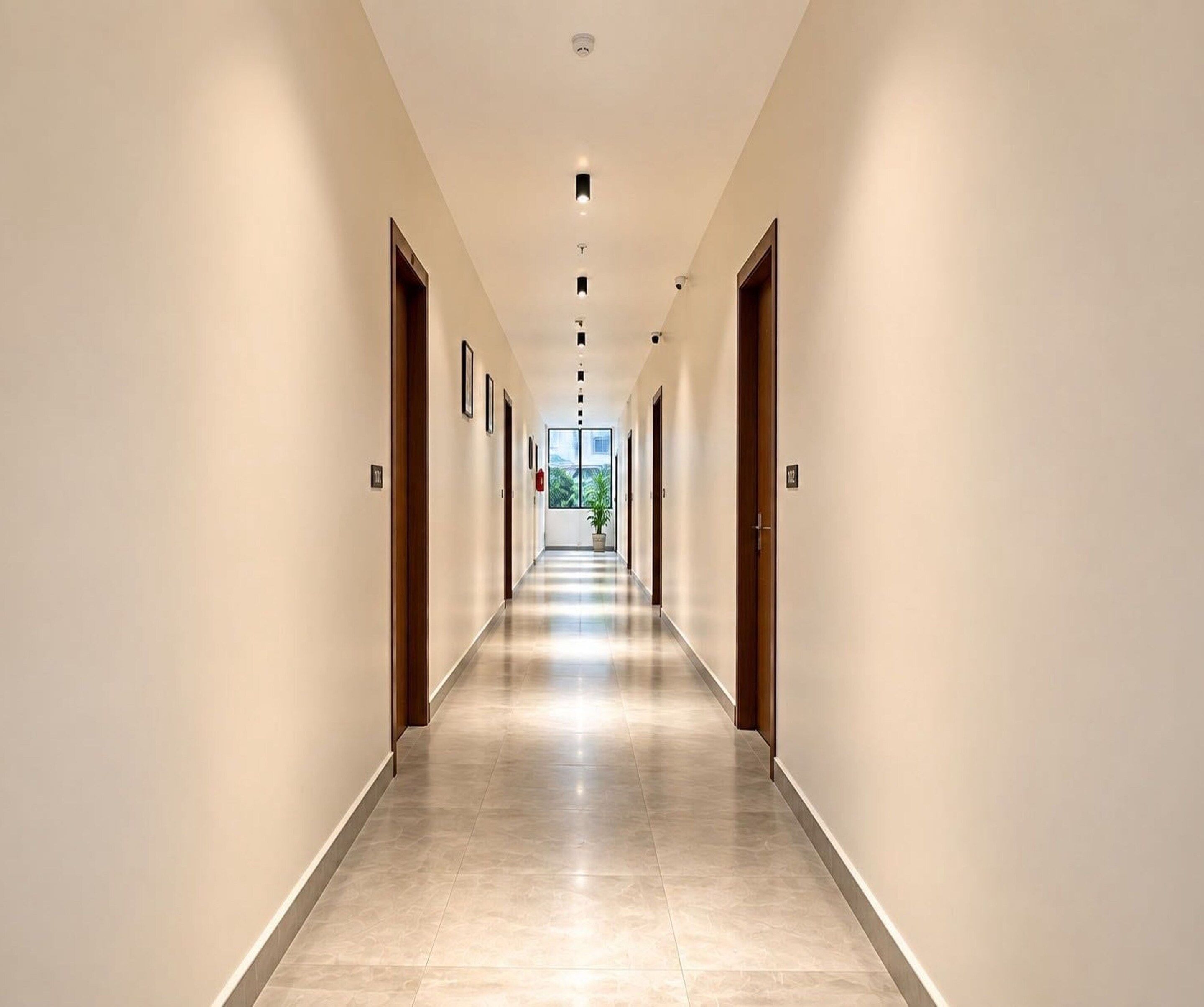 A long, narrow hotel corridor with doors on both sides, a tiled floor, and recessed lighting on the ceiling.