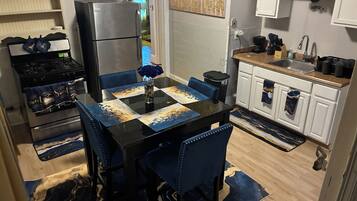 A modern kitchen with a black dining table, blue chairs, and a refrigerator.