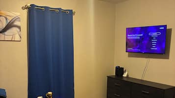 A bedroom with a bed, a dresser, a TV on the wall, and a nightstand with a lamp.