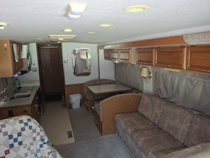 A compact RV interior with a kitchenette, a dining area, and a seating area.