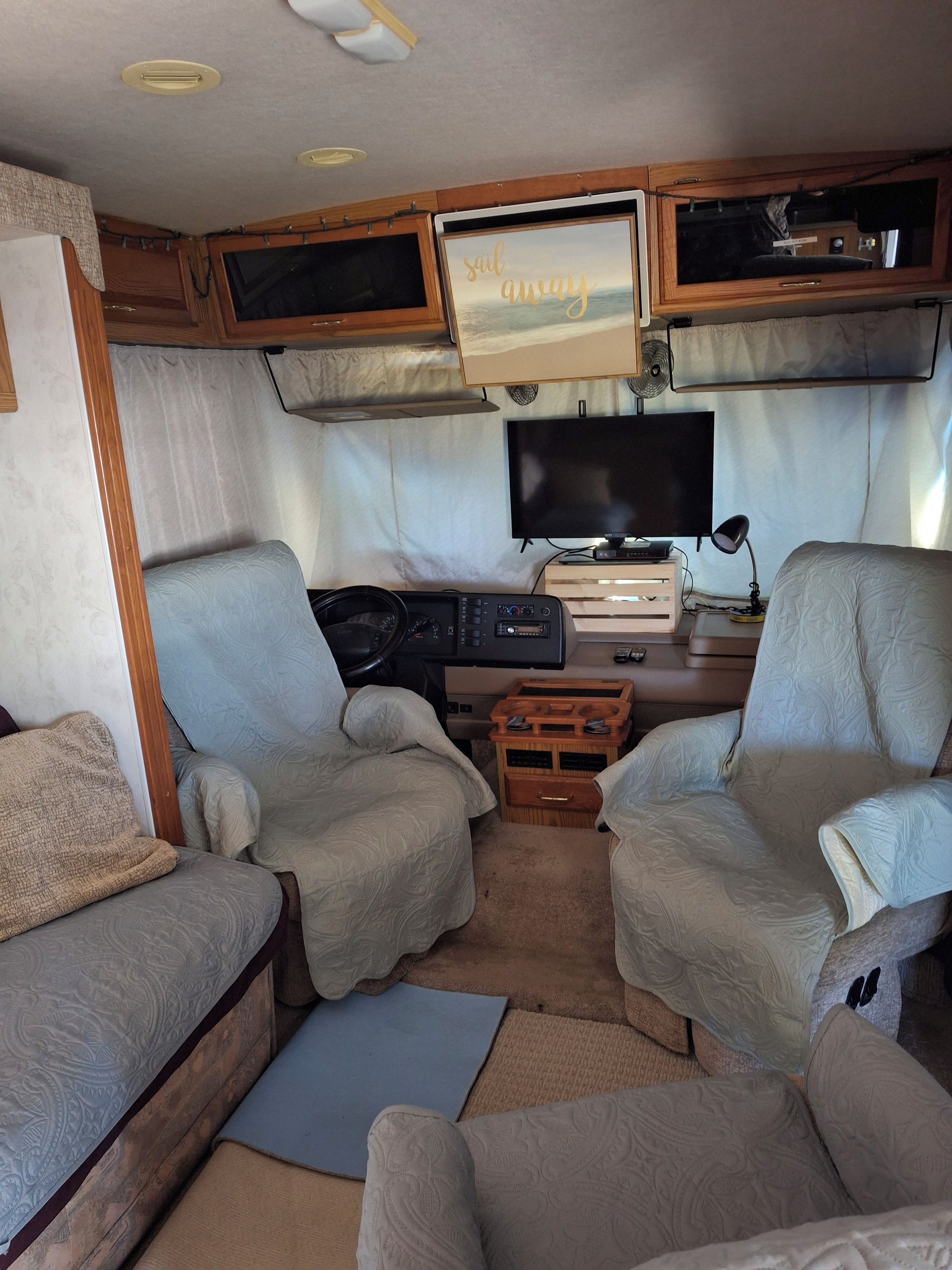 Un interior de autocaravana acogedor con dos sillones, un televisor y un mueble de entretenimiento pequeño.