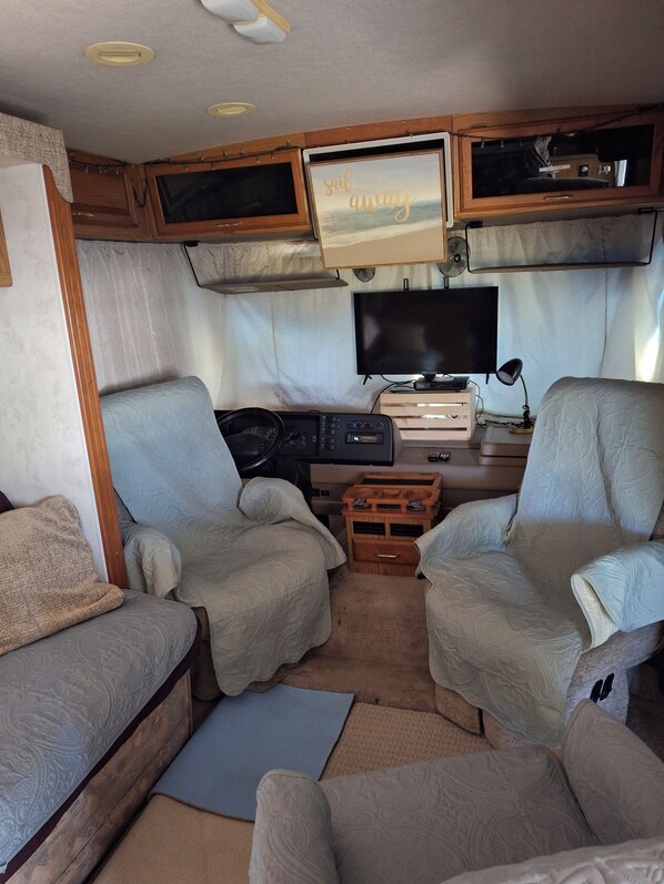 Interior acollidor d'una caravana amb dos seients còmodes, una televisió i un petit moble d'entreteniment.