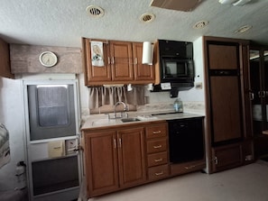 A compact RV kitchen with wooden cabinets, a sink, a microwave, and a refrigerator.