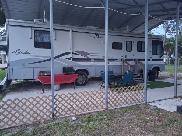 A recreational vehicle with a covered area, a table, and chairs.