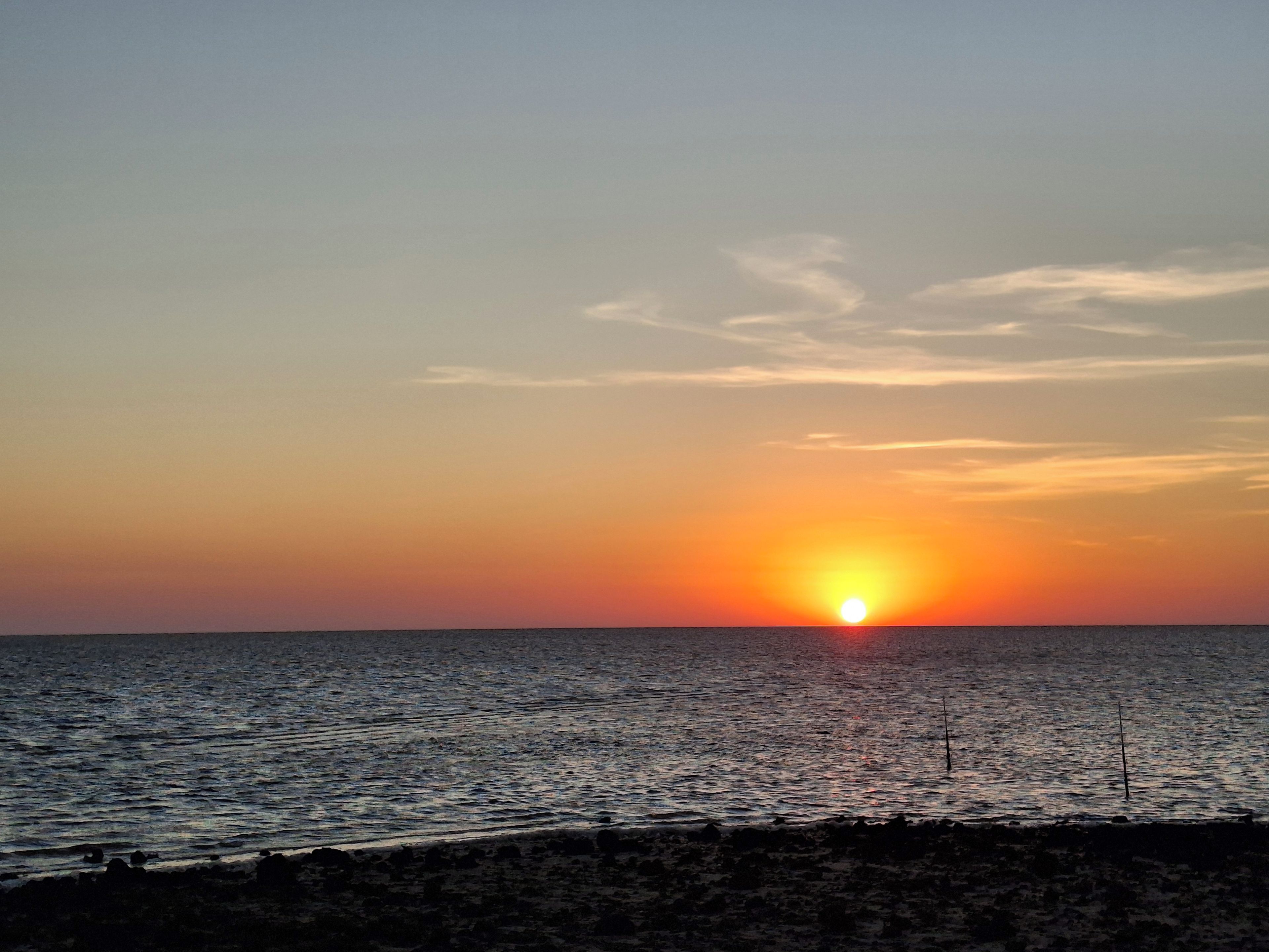 Un coucher de soleil sur une mer calme, avec une côte rocheuse.