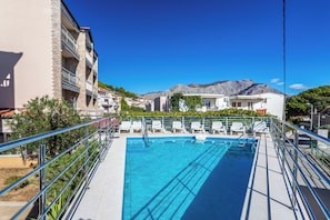 A swimming pool with a view of a mountain and residential buildings in the background. - A6 - Spacious apartment with pool, 5 balconies and the sea view, near beach (Omiš)
