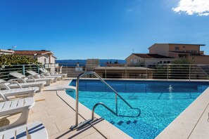 En swimmingpool med en metalstige, liggestole og havudsigt.