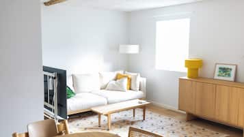 A minimalist living room with a sofa, a coffee table, a wooden cabinet, and a window providing natural light.