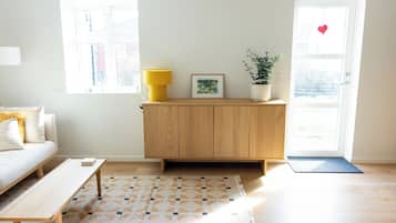 Una sala de estar con un sofá, un armario de madera, una lámpara amarilla, un cuadro enmarcado y una planta en maceta.