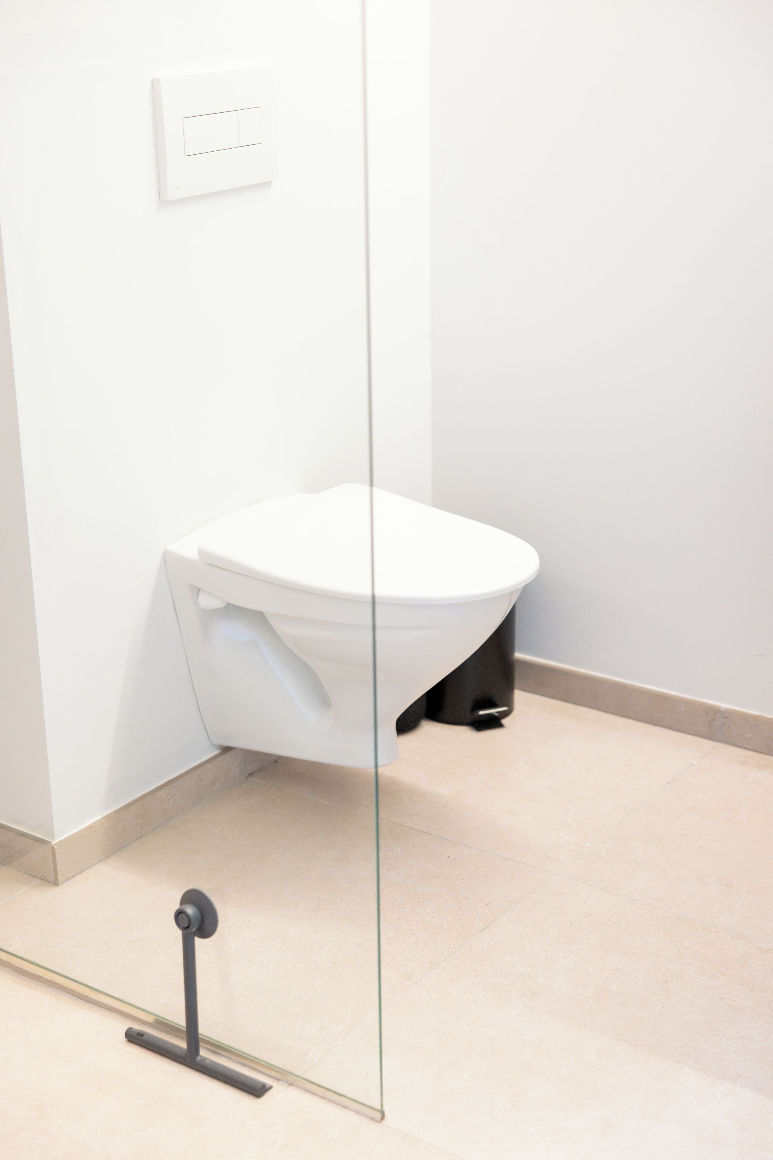 A white toilet with a black base, a glass partition, and a light switch on the wall.