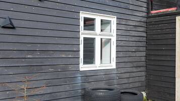 A house with a dark exterior, a white window, and a small garden with yellow flowers and tires used as planters.