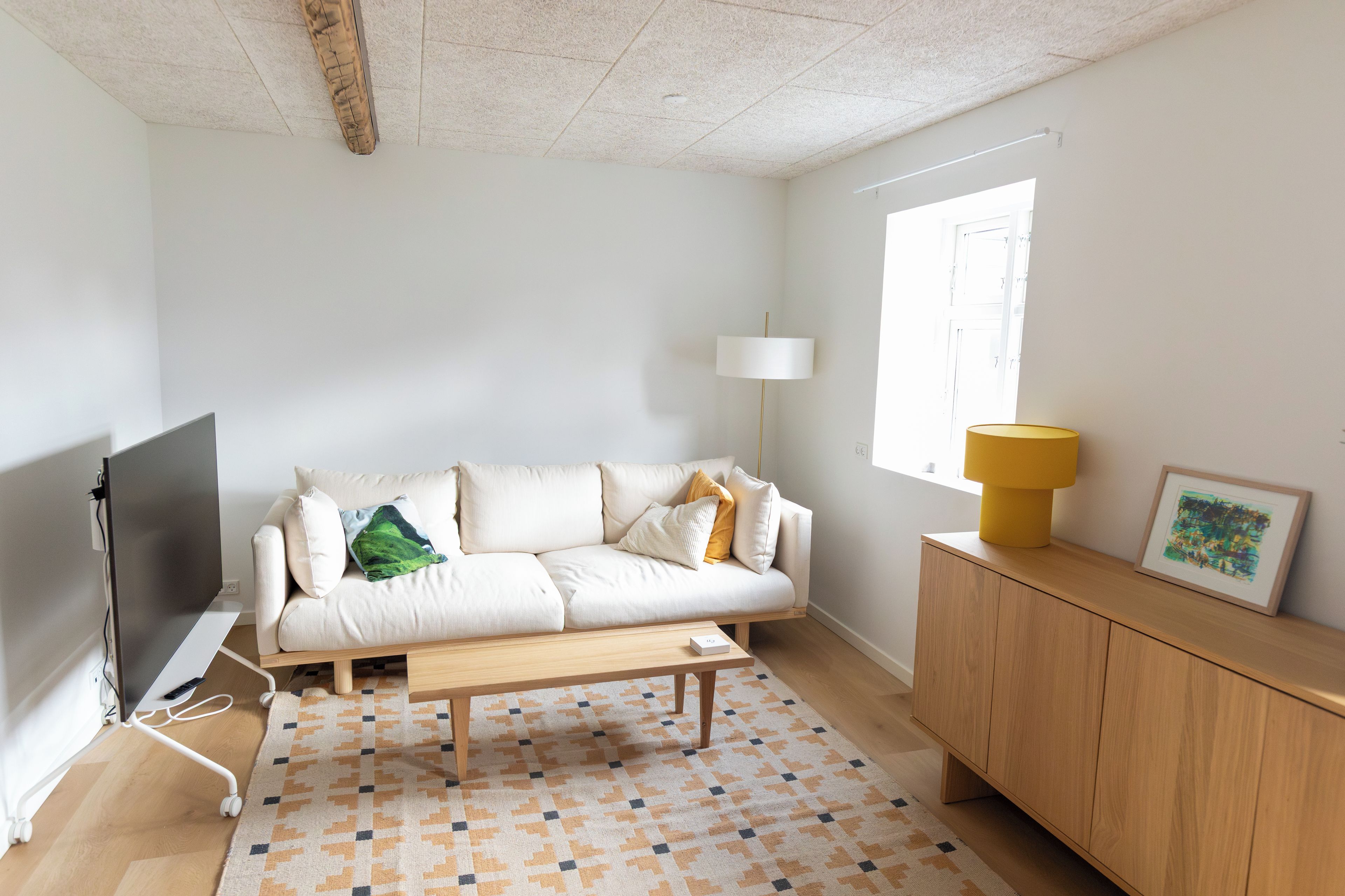 A modern living room with a sofa, a coffee table, a TV, a lamp, a window, and a cabinet.