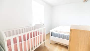 A room with a crib, a bed, and a wooden cabinet.