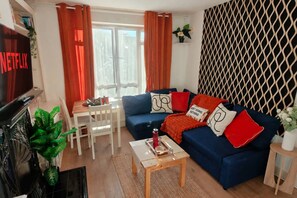 A living room with a blue sofa, red cushions, a coffee table, a TV, and a window with curtains. - Ladbroke Grove 1 Bed Flat | Fast Wi‑Fi | Sleeps 4 (Greater London)