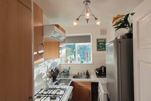Eine kleine Küche mit Gasherd, Spüle und Kühlschrank.