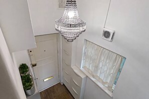 A narrow hallway with a chandelier, a door, a window with curtains, and a small potted plant. - Ladbroke Grove 1 Bed Flat | Fast Wi‑Fi | Sleeps 4 (Greater London)