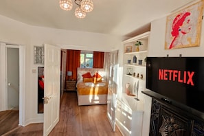 Ein Hotelzimmer mit Bett, Fernseher und einem zur anderen Kammer führenden Flur.