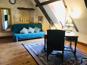 A cozy room with a wooden floor, a blue sofa, a black chair, and a table with a lamp. - Under skies that arch from field to forest (Saint-Cernin-de-Labarde)