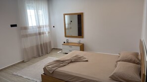 A bedroom with a bed, a bedside table, a mirror, and a window with curtains. - Modern 2-Bedroom Apartment with Balcony Near the Beach (Sousse)