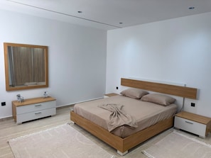 A modern bedroom with a wooden bed frame, a bedside table, a nightstand, a mirror, and a small dresser. - Modern 2-Bedroom Apartment with Balcony Near the Beach (Sousse)