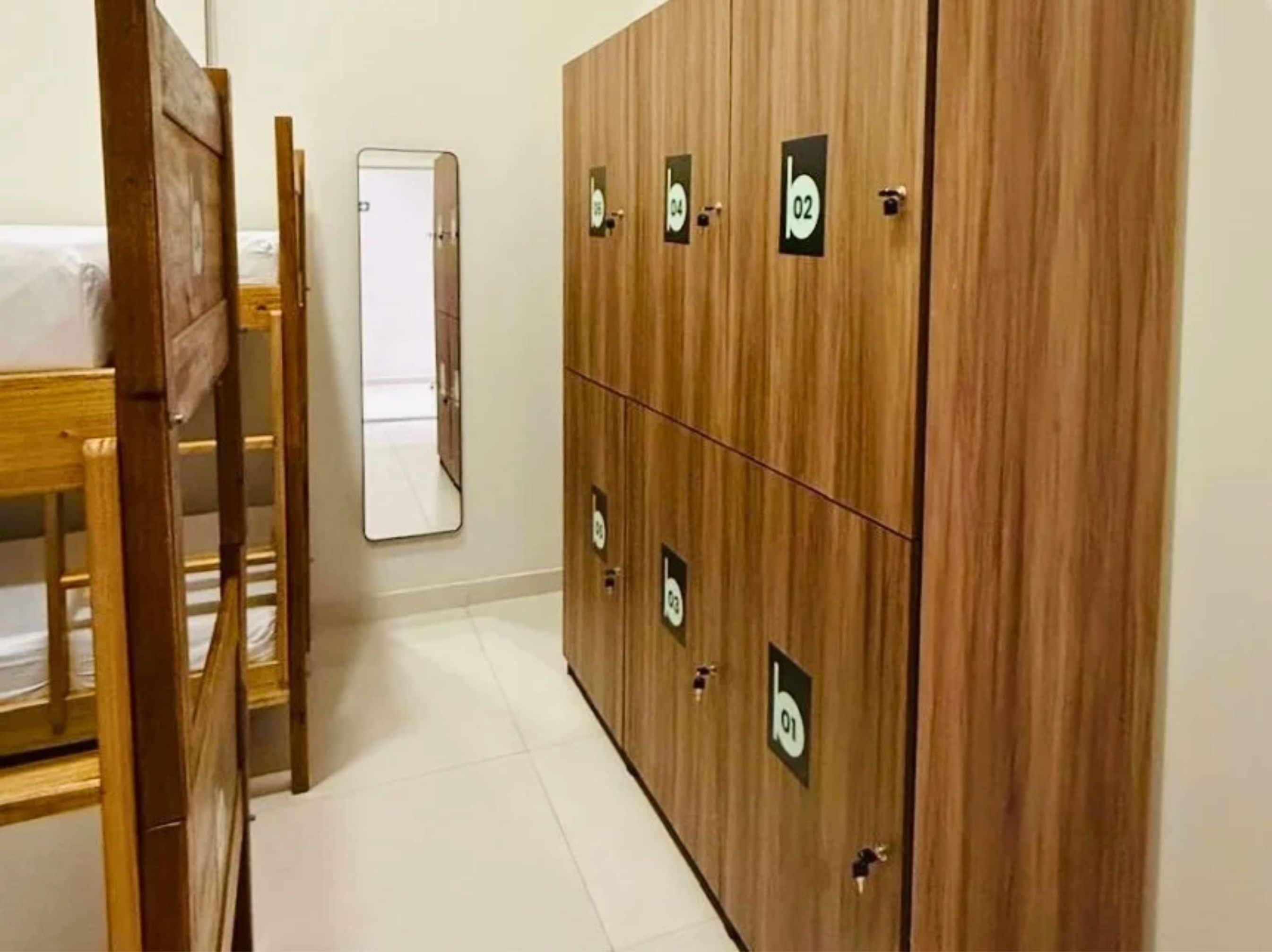 A room with wooden bunk beds, a wooden wardrobe with numbered compartments, and a mirror on the wall.