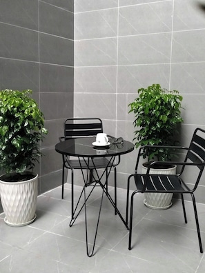 Un petit espace extérieur moderne, aménagé avec une table ronde et deux chaises, le tout entouré de plantes en pot.