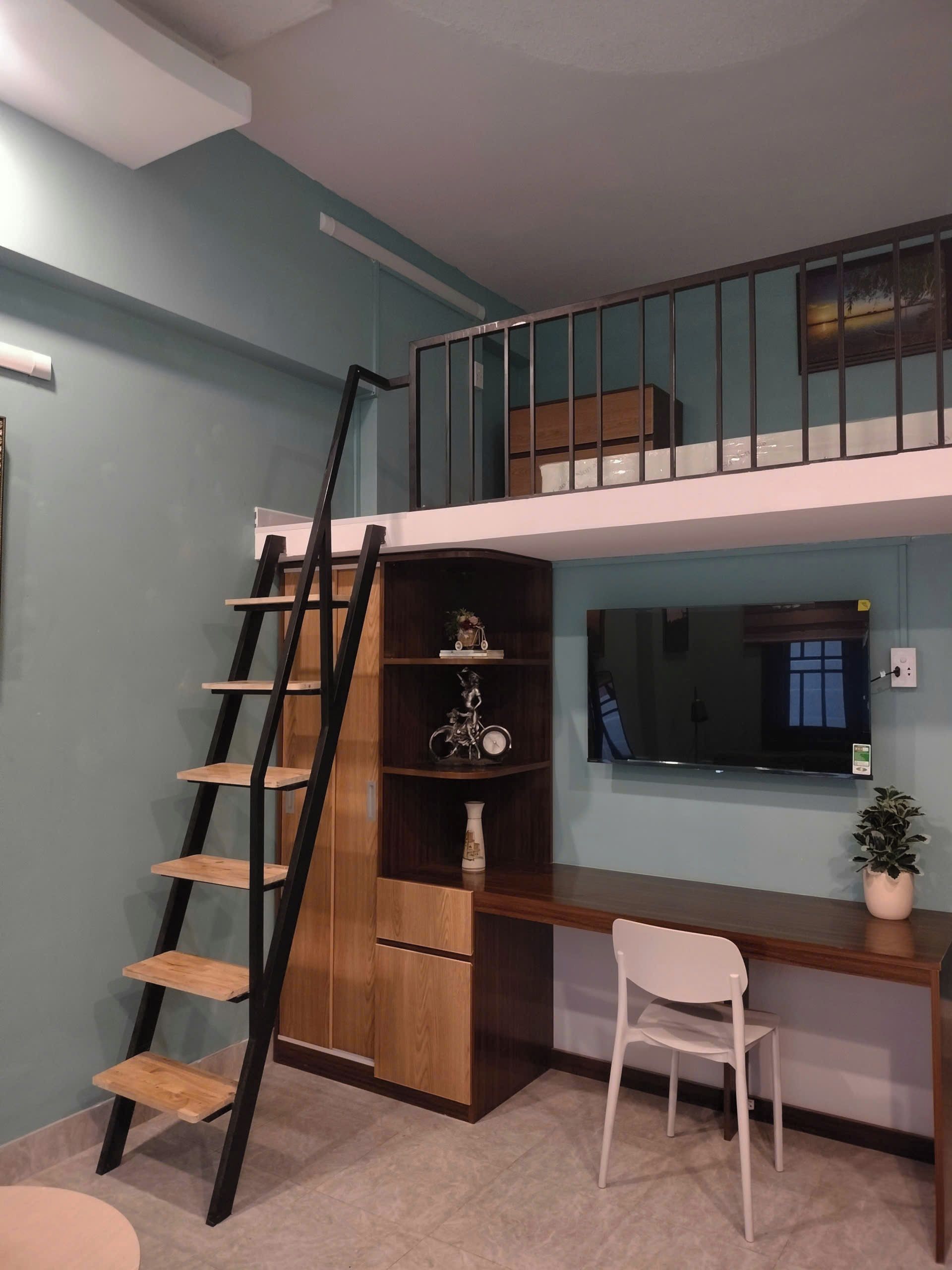 Une pièce avec un bureau en bois, une chaise blanche, un téléviseur, une bibliothèque et un escalier menant à un niveau supérieur.