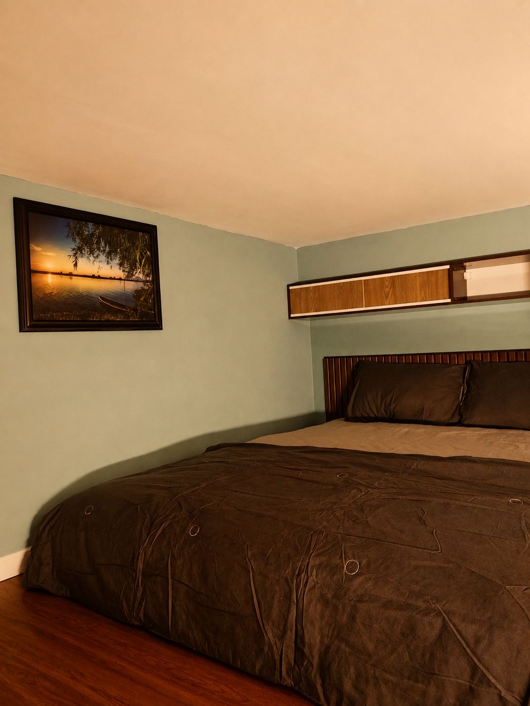 Une chambre à coucher avec un lit, une table de chevet, une étagère fixée au mur et un tableau encadré.