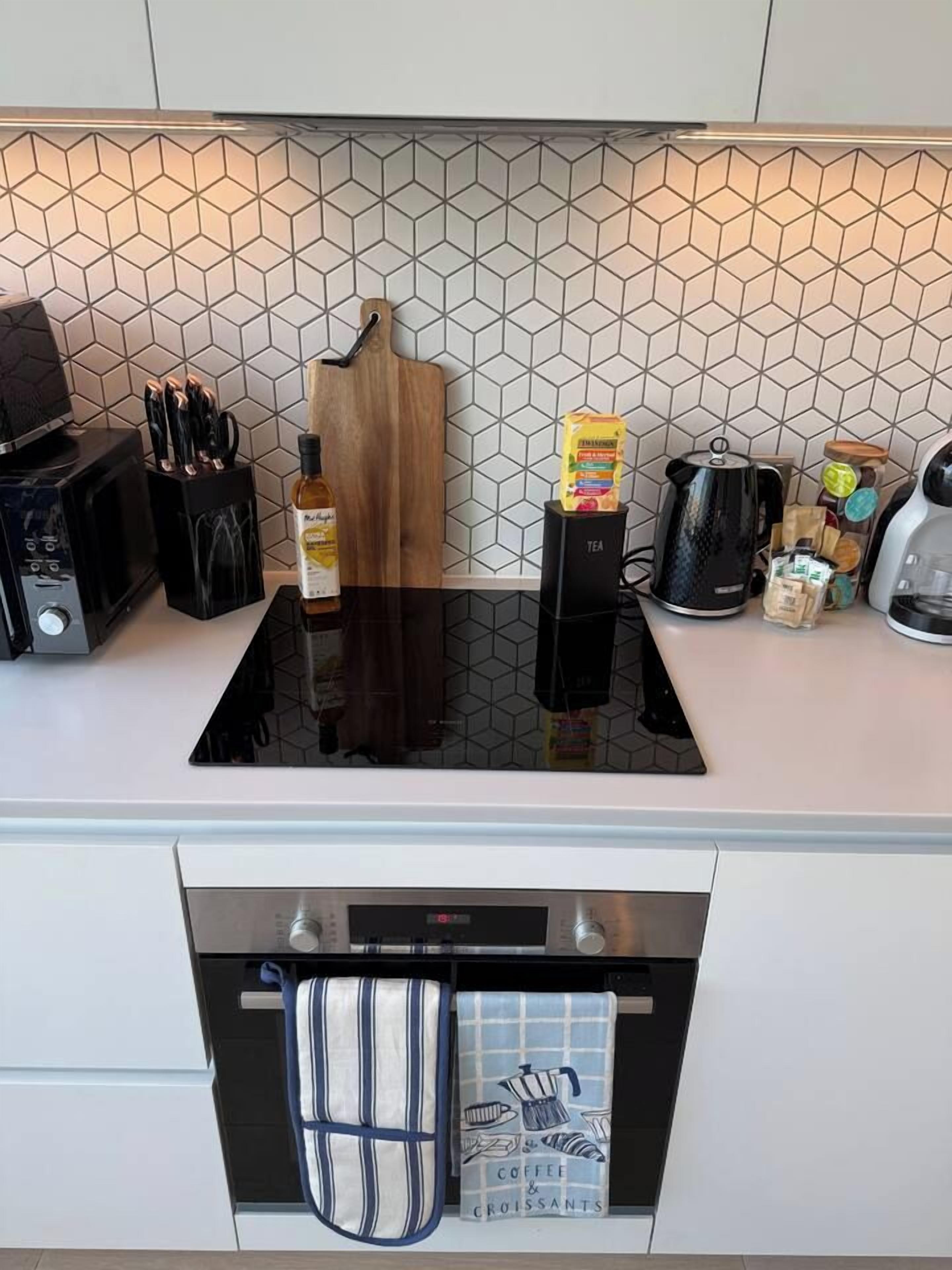 Eine Küche mit einem schwarzen Induktionskochfeld, einer Mikrowelle, einem Messerblock, einem Holzschneidebrett, einem Wasserkocher und einer Kaffeemaschine.
