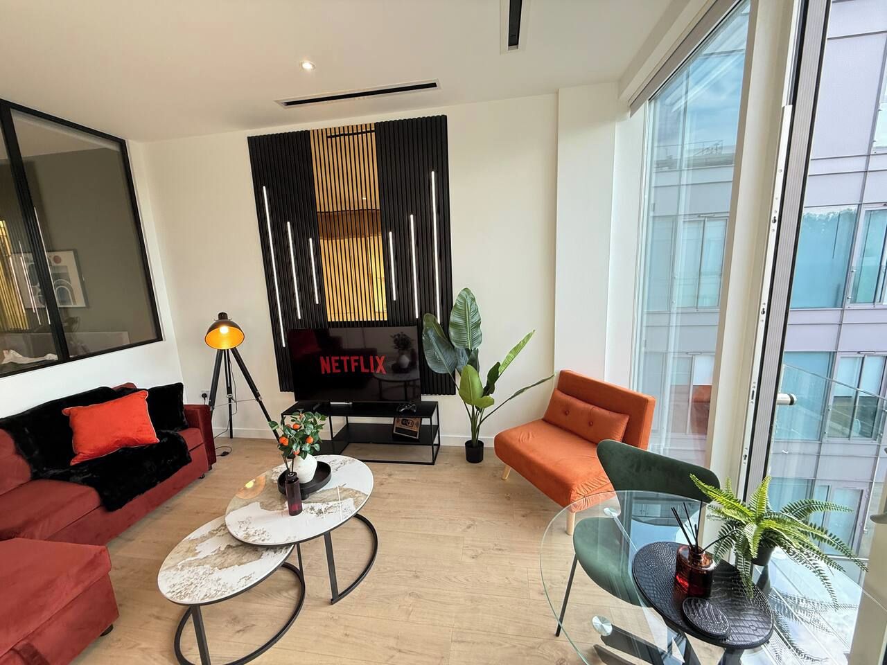 A modern living room with a flat-screen TV, a red sofa, an orange armchair, and a glass coffee table.