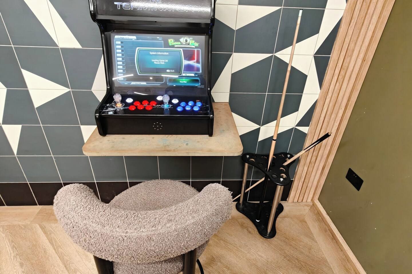 Et billardbord med digitalt resultatdisplay, et billjardkø-stativ og en polstret stol.