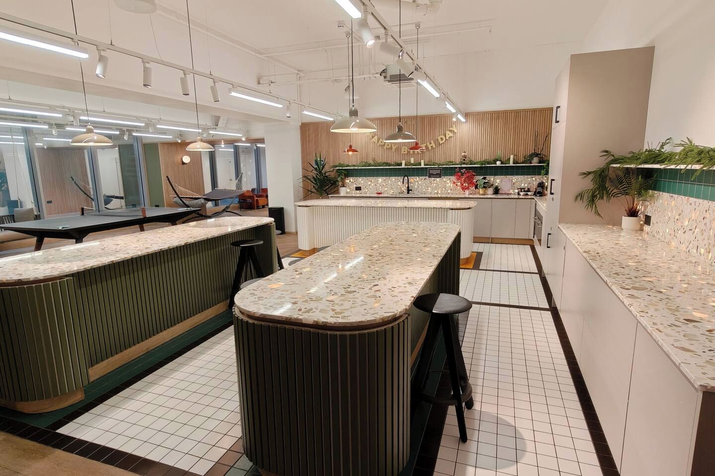 Una cocina moderna con una isla central, asientos tipo bar, iluminación colgante y un letrero que dice 'Happy Birthday'.