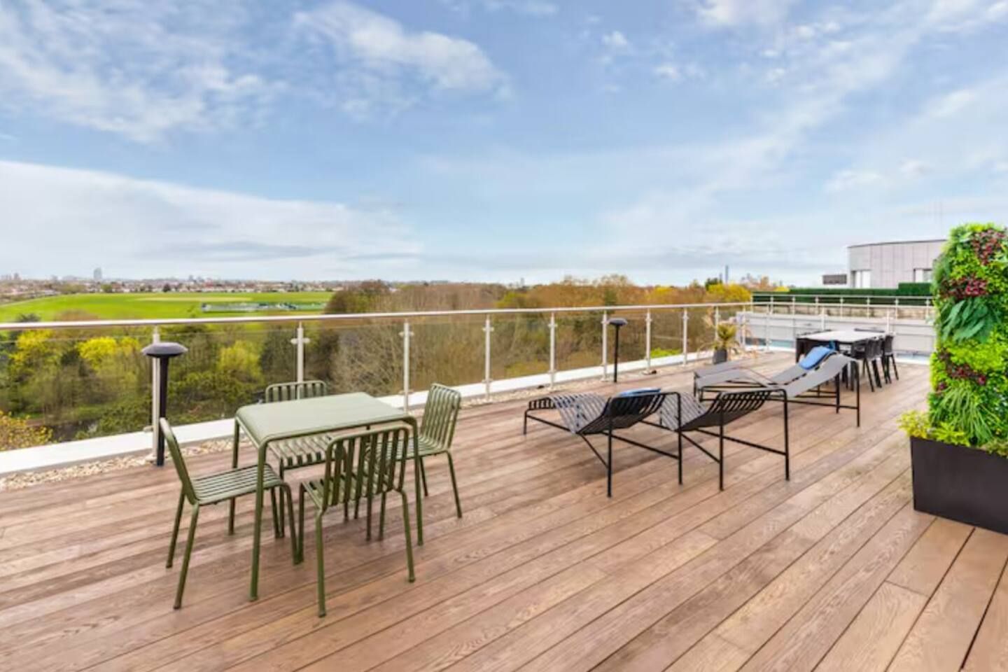A wooden deck with outdoor furniture, a view of the countryside, and a building with a green wall.