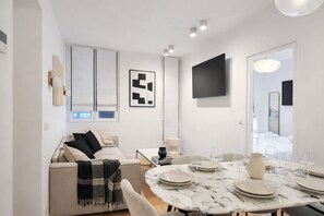 A modern living room with a sofa, a dining table set for four, and a TV mounted on the wall. - Comfortable Air-conditioned Apartment - East Paris (Paris)