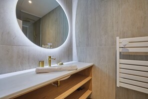 A modern bathroom with a round mirror, a white countertop, a gold faucet, and a towel rack. - Comfortable Air-conditioned Apartment - East Paris (Paris)
