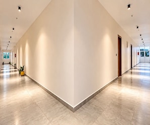 A long, well-lit corridor with a tiled floor, potted plants, and doors on one side. - Classic V Stays (Chittoor)