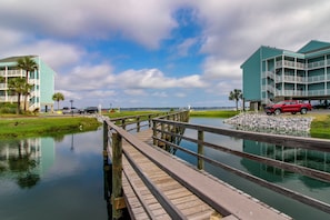 A waterfront property with a wooden dock leading to a calm body of water, surrounded by greenery and a clear sky. - Unwind Poolside, Walk to Beach! Pensacola Getaway (Pensacola Beach)