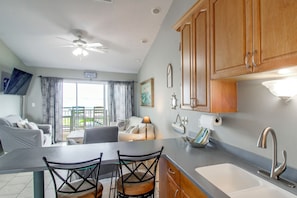 A kitchen with wooden cabinets, a sink, and a ceiling fan. There is a dining area with a table and chairs. - Unwind Poolside, Walk to Beach! Pensacola Getaway (Pensacola Beach)