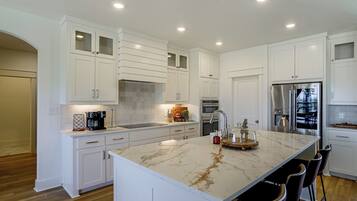 A modern kitchen with white cabinetry, a marble island, and stainless steel appliances.