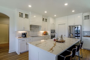 Una cocina moderna con armarios blancos, una isla de mármol y electrodomésticos de acero inoxidable.