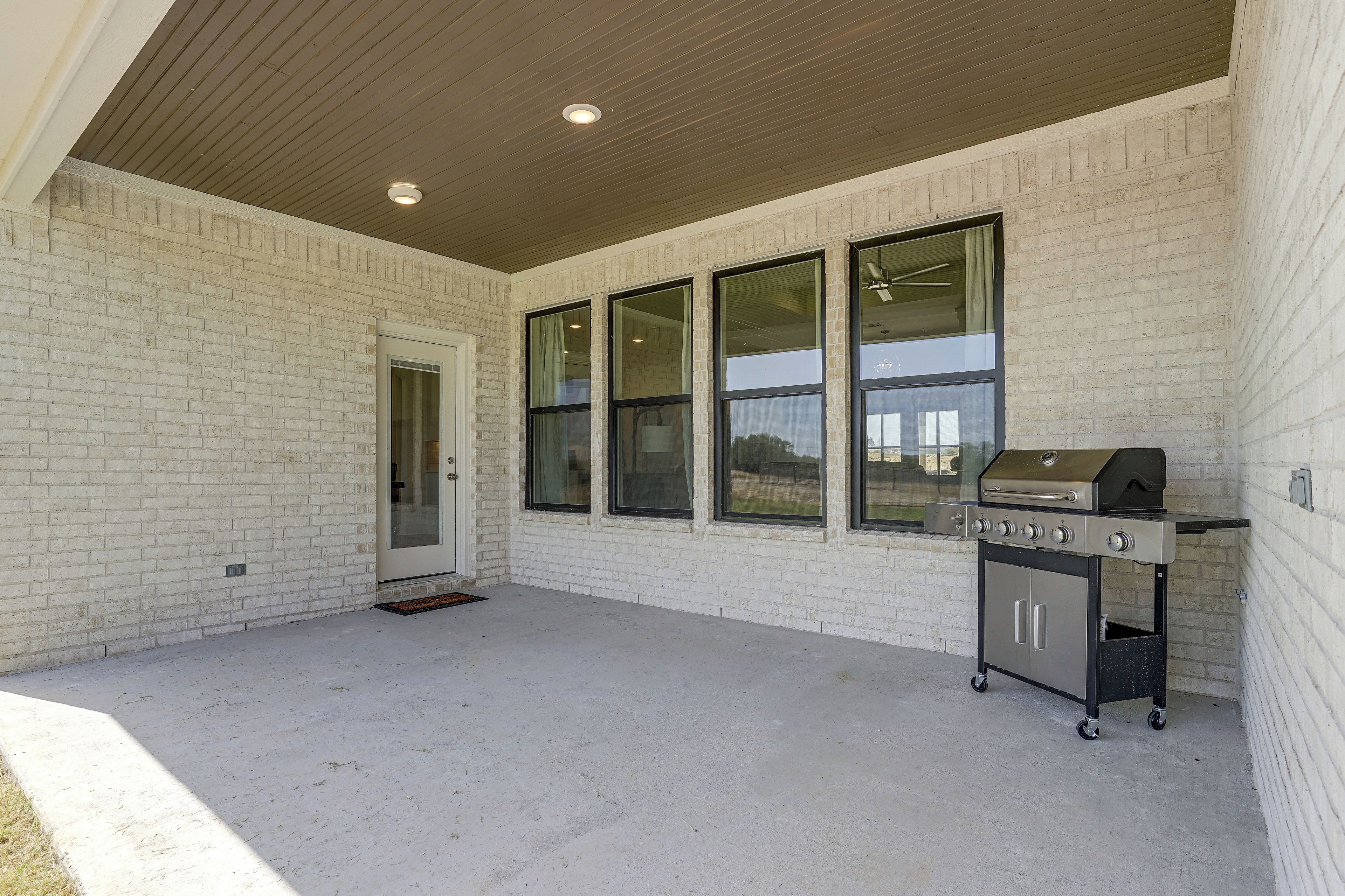 Un patio couvert avec un barbecue, de grandes fenêtres et une porte.