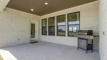 Un patio couvert avec un barbecue, de grandes fenêtres et une porte.
