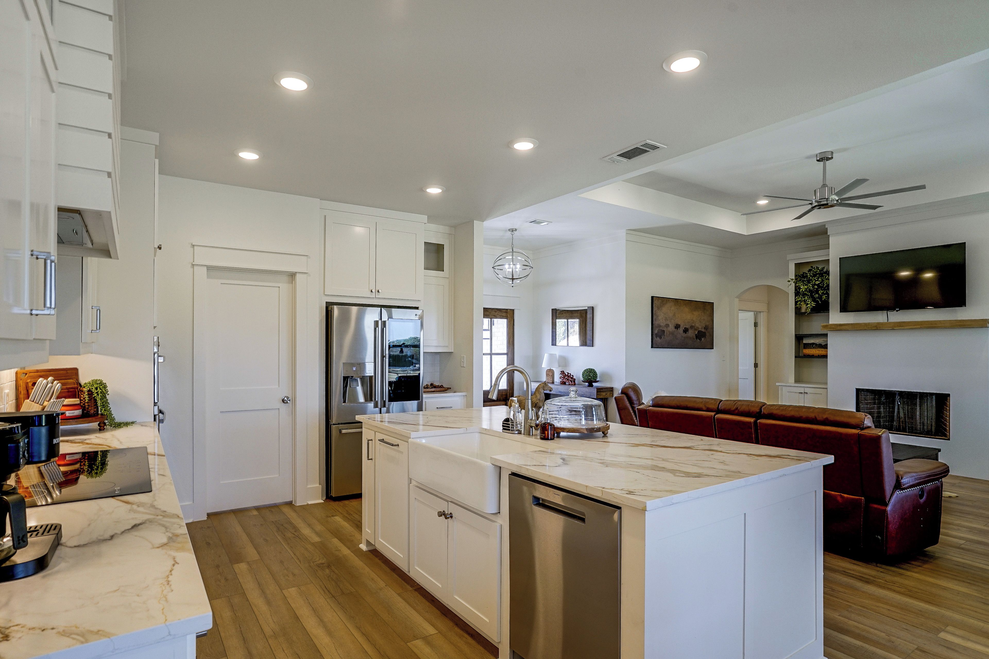 A modern kitchen with white cabinetry, a built-in island, stainless steel appliances, and a ceiling fan.