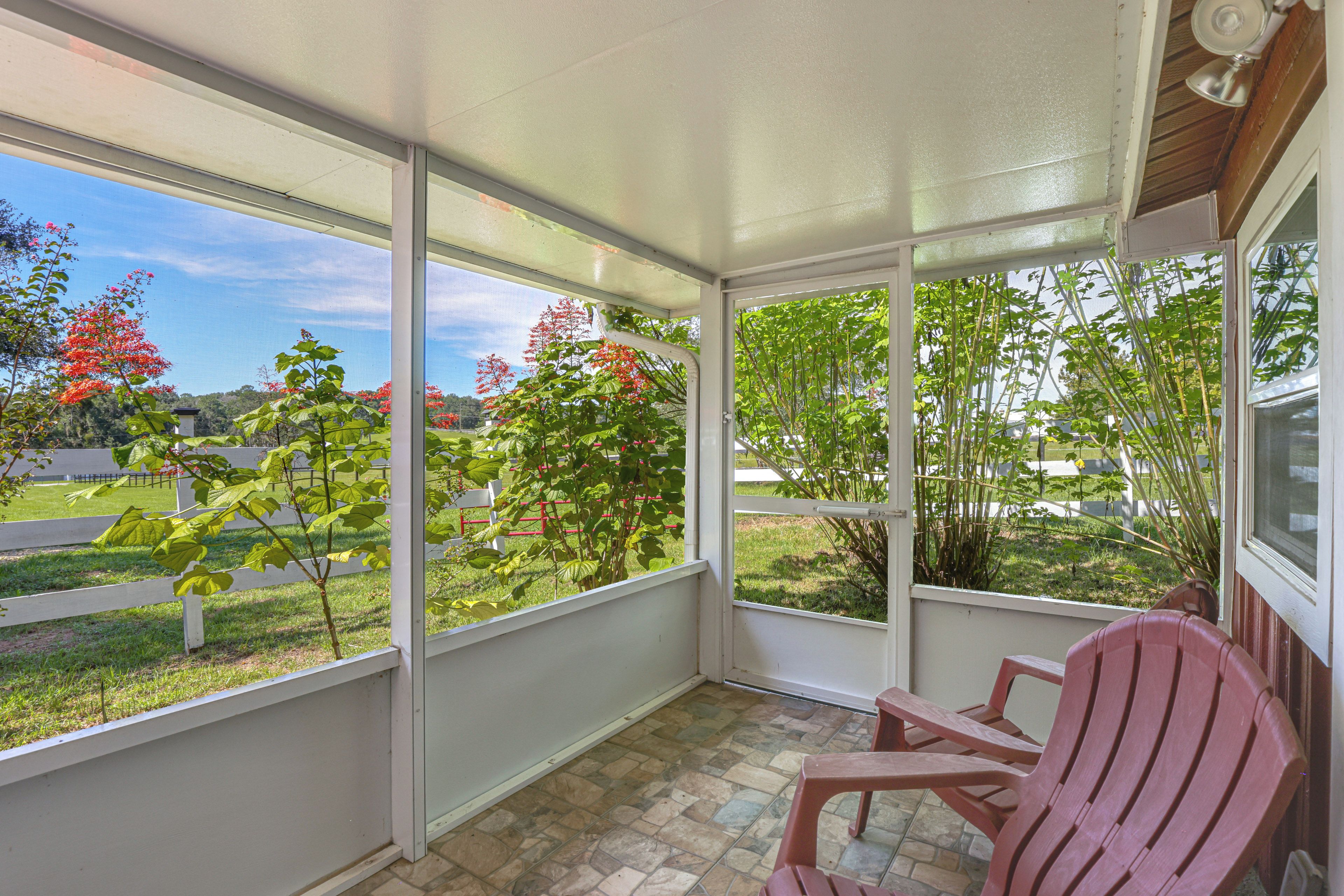 A covered patio area with a view of a garden and a red chair.