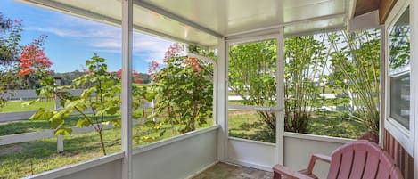 A covered patio area with a view of a garden and a red chair.
