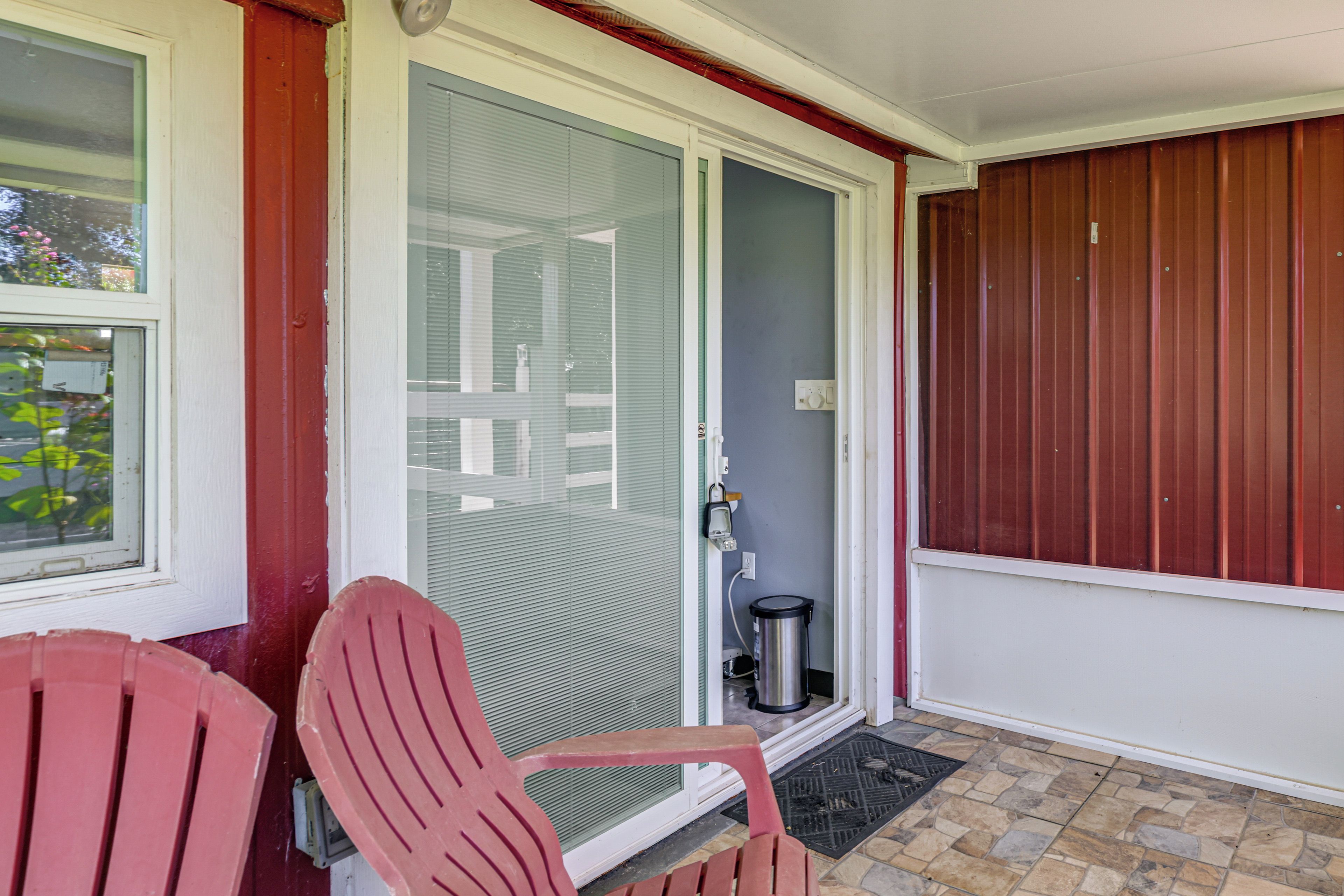 A covered porch with two red chairs, a door with a glass panel, and a metal trash can.