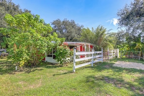 A rustic cabin with a red exterior, surrounded by lush greenery and a white fence. - 6 Mi to Spanish Springs! Private Unit w/ Projector (Lady Lake)